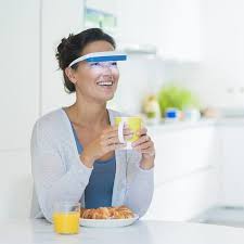 Woman in a kitchen holding a glass of orange juice and a plate of food while wearing Luminette 3 Light Therapy Glasses