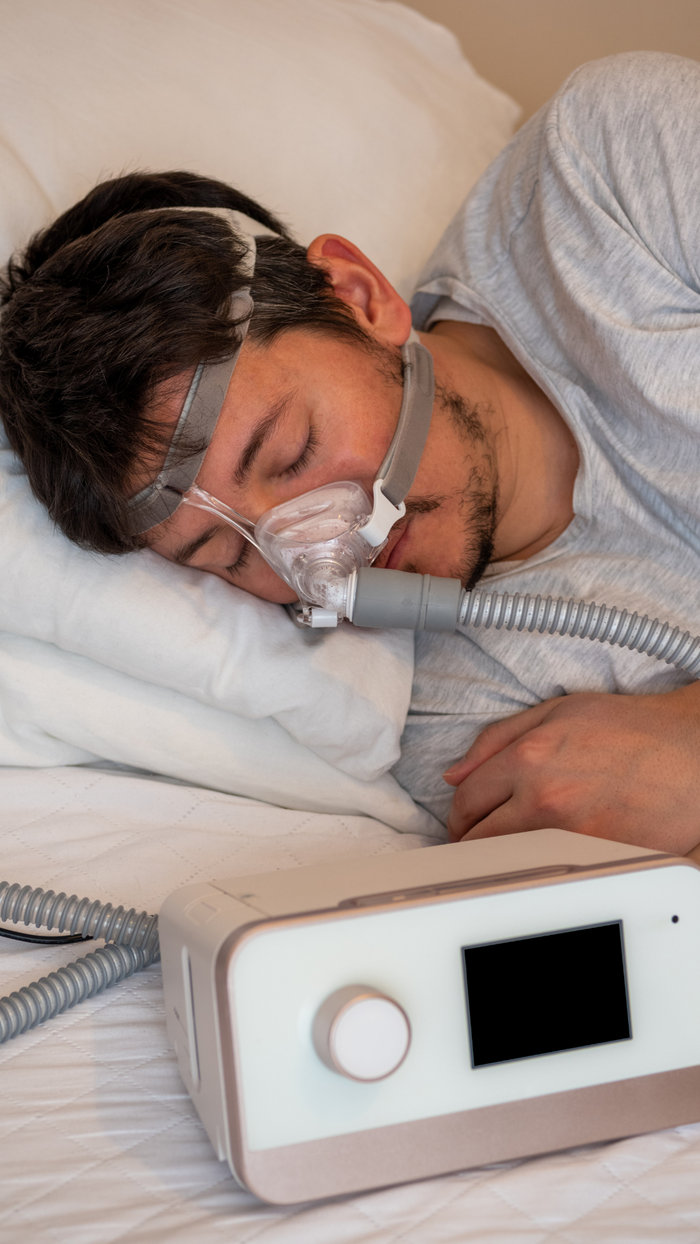 Person using a CPAP machine to sleep with a visible CPAP device on a bed.