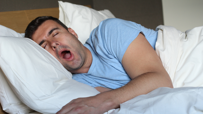 Man yawning in bed with white pillows and bedding